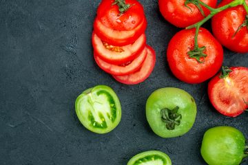 зеленые и красные помидоры, нарезанные и целые, на темном фоне