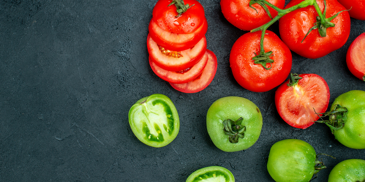 зеленые и красные помидоры, нарезанные и целые, на темном фоне