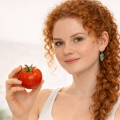 Рыжая кудрявая девушка держит в руке помидор