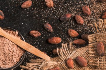 Какао-бобы, мешковина, порошок какао в круглой миске и деревянная ложка