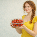 Девушка в жёлтом платье держит в руках пластиковый контейнер с клубникой