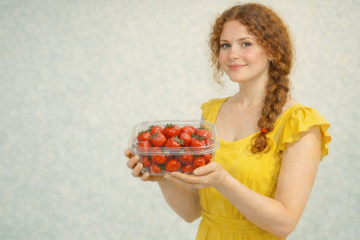 Девушка в жёлтом платье держит в руках пластиковый контейнер с клубникой