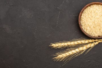 Зерна пшеницы в круглой миске и колосья пшеницы на темном фоне