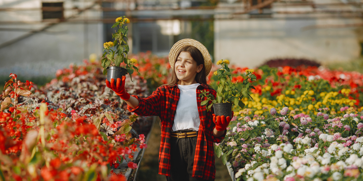 девочка в соломенной шляпе держит горшки с цветами в теплице