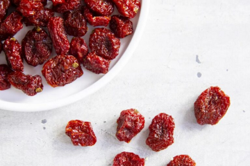 В круглой белой миске лежат вяленные помидоры черри, несколько лежит рядом с миской