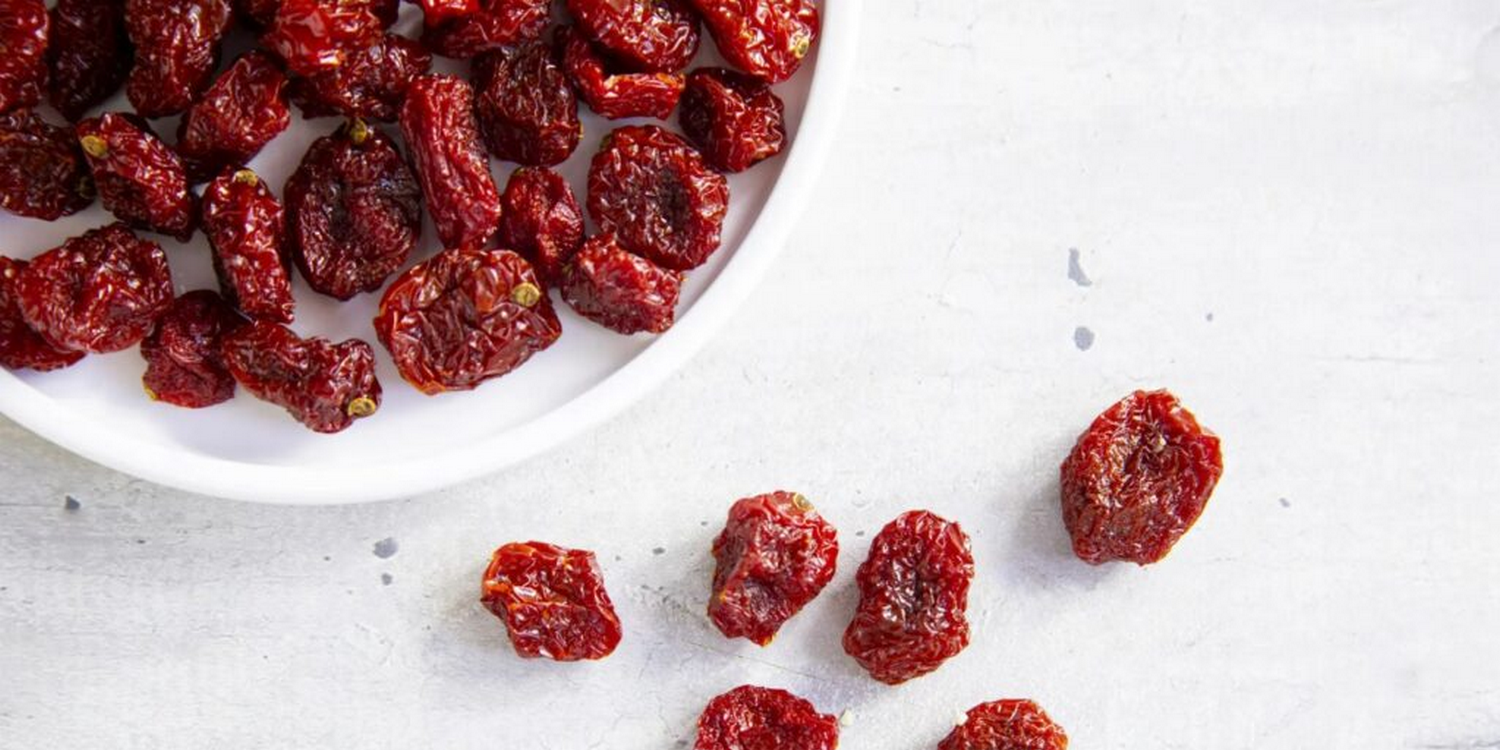 В круглой белой миске лежат вяленные помидоры черри, несколько лежит рядом с миской