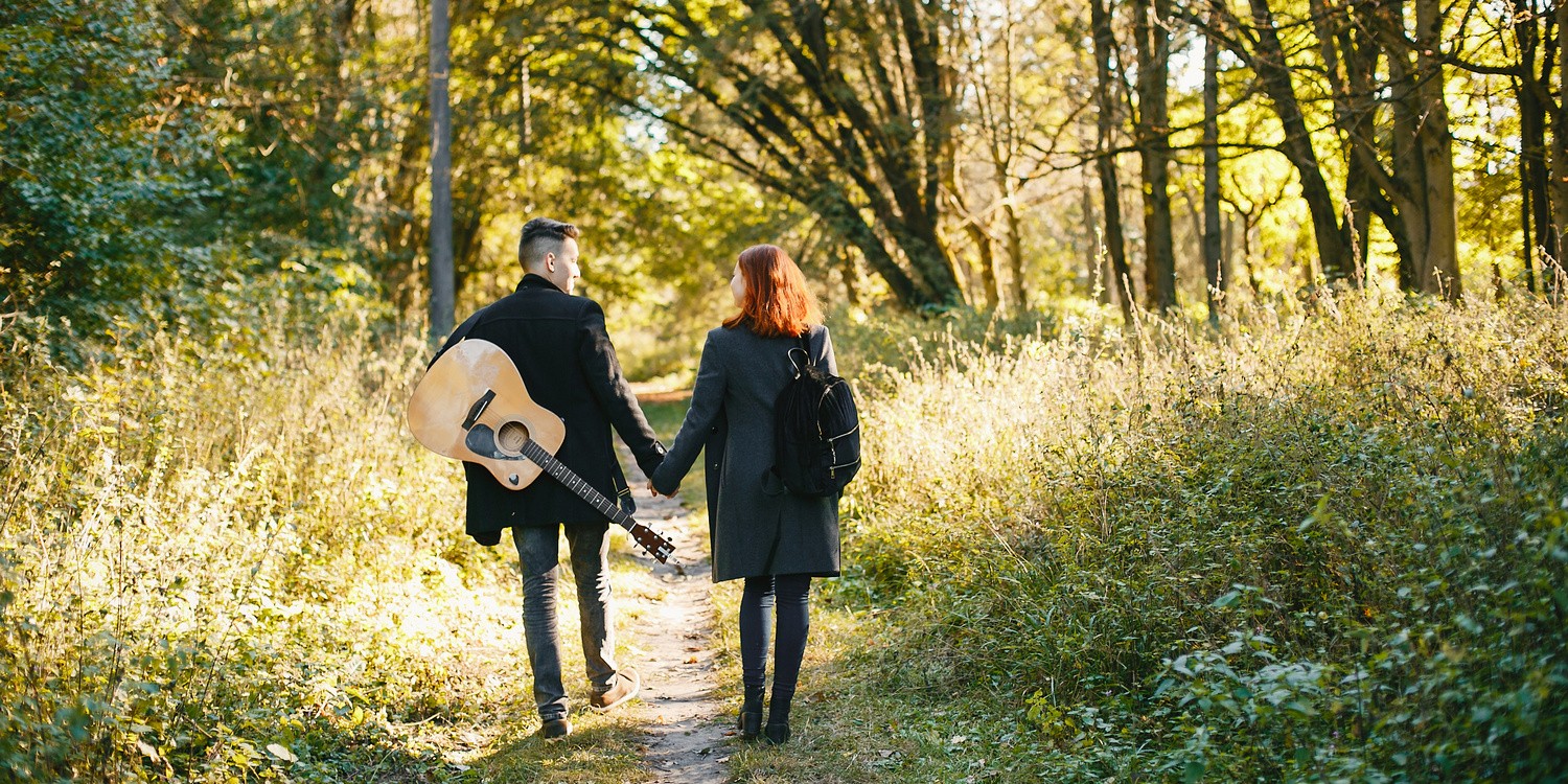 Девушка и молодой человек с гитарой гуляют в парке