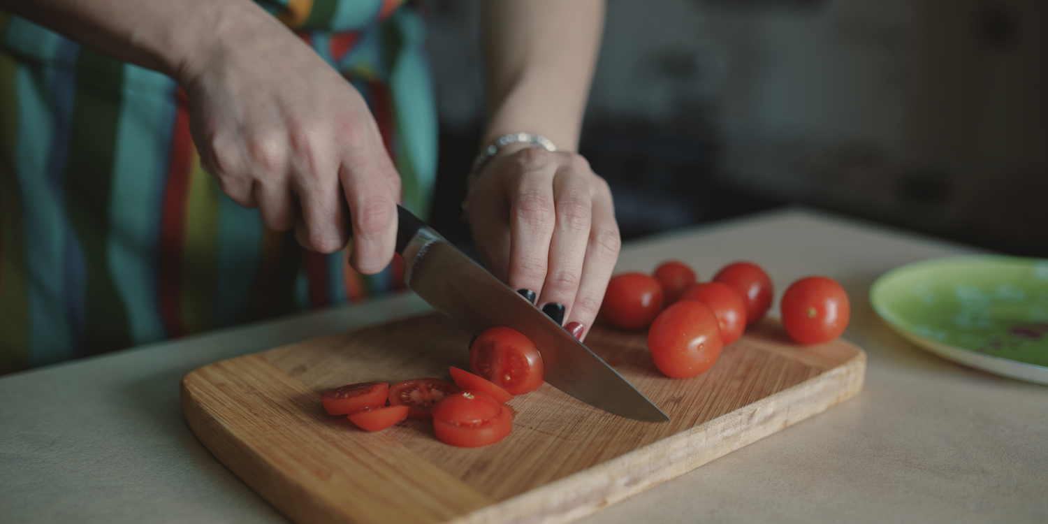 Женщина нарезает томаты на разделочной доске, крупным планом
