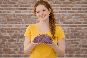 Девушка в жёлтой футболке держит в руках разрезанный каравай фиолетового хлеба