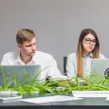 Молодые сотрудники компании работают за ноутбуками в окружении растений