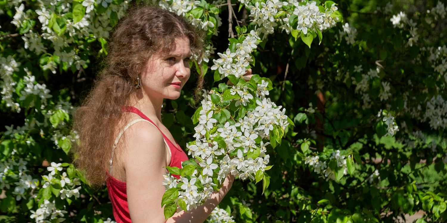 Девушка в красной майке стоит рядом с цветущей яблоней