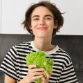 Девушка стоит на кухне с листовым салатом в руках
