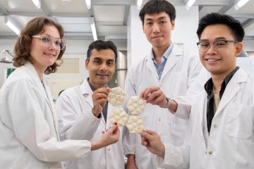 Четыре ученых в белых халатах демонстрируют шестиугольные плитки из мицелия