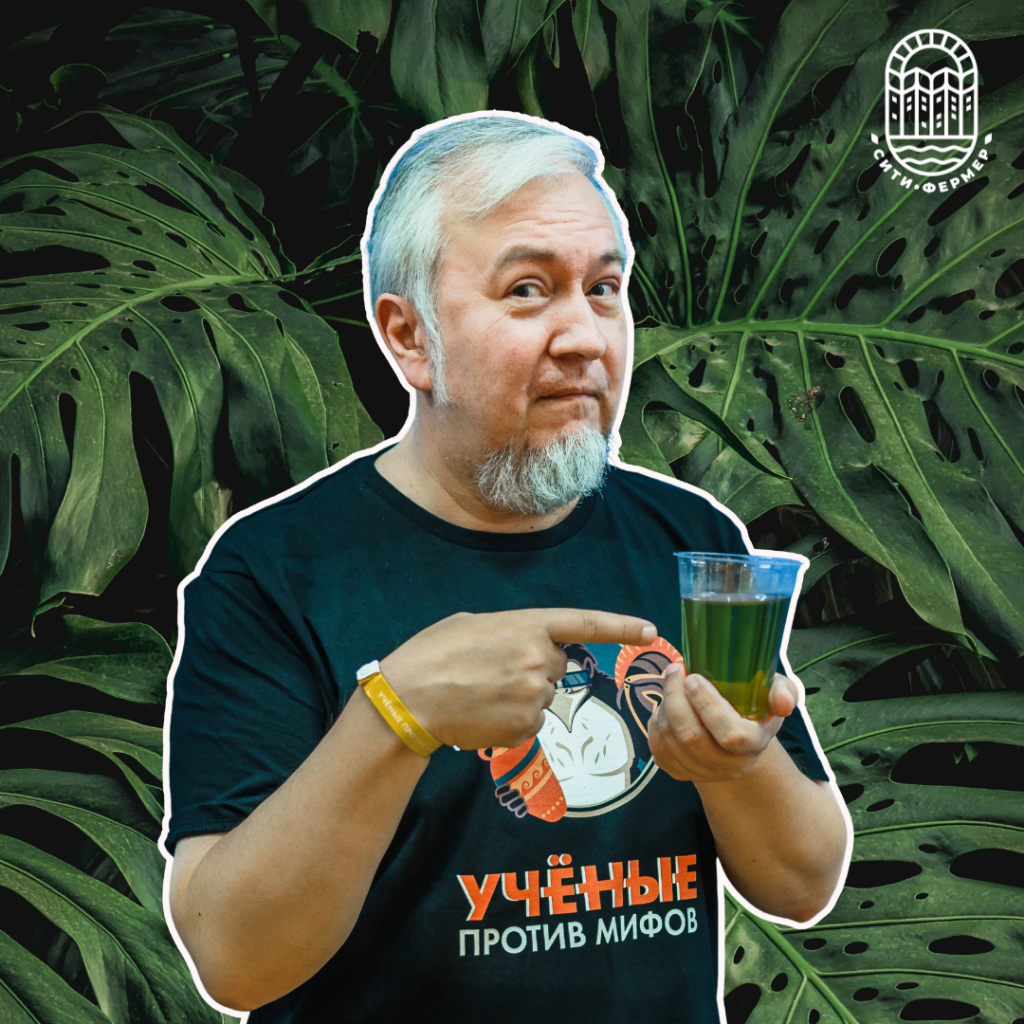 Алексей Водовозов показывает стакан с зелёной жидкостью, который держит в руках