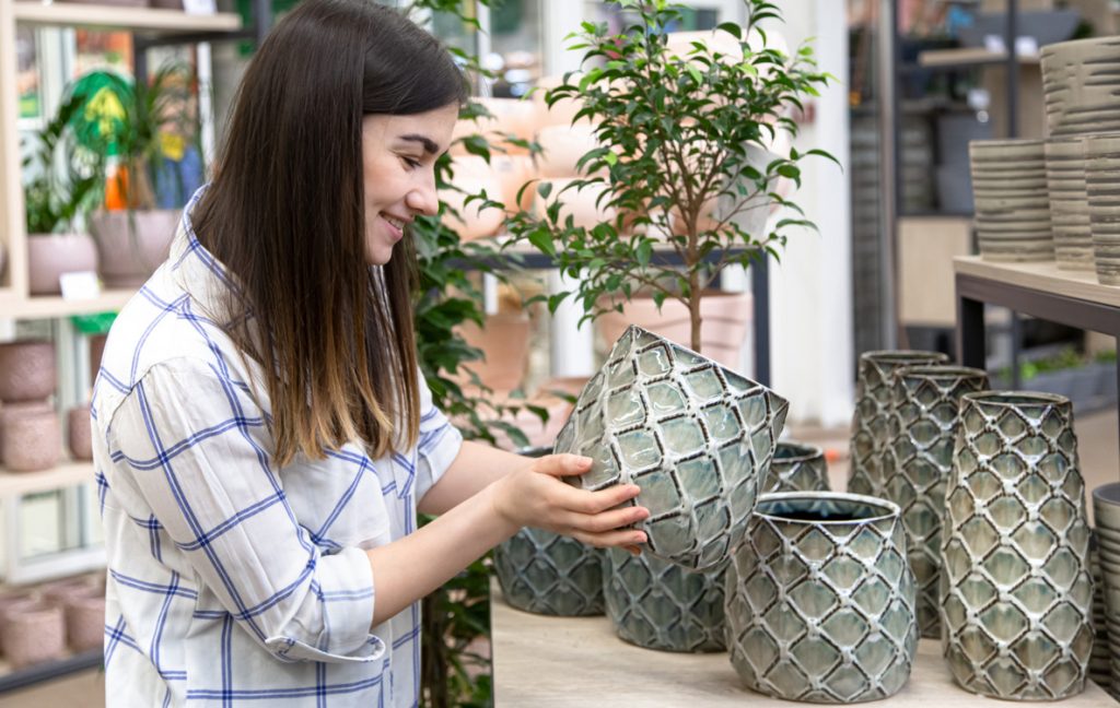 Молодая женщина рассматривает горшки для цветов разной формы в магазине