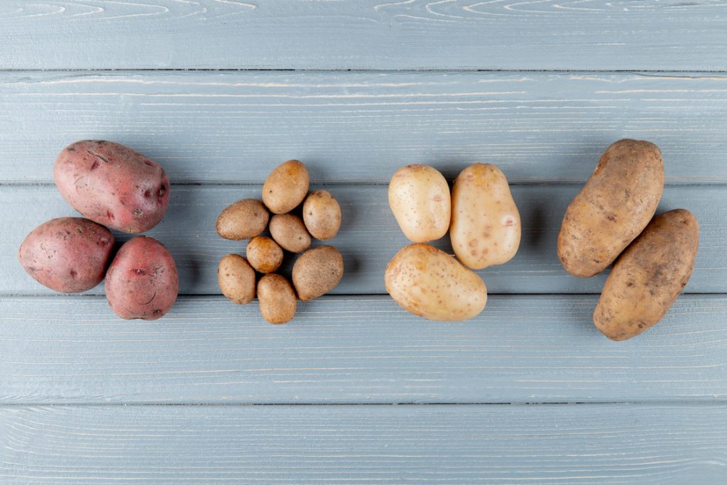 На голубом деревянном столе лежит четыре сорта картошки