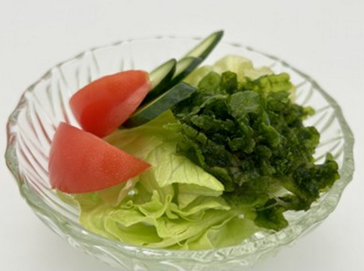 В небольшом хрустальном салатнике лежит овощной салат: нарезаны помидор, огурец, листовой салат и маршанция изменчивая