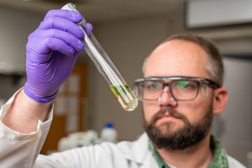 Учёный в белом халате и очках рассматривает пробирку с растением